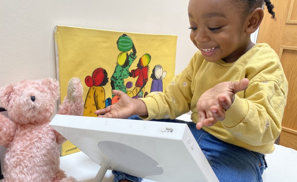 toddler talking to family through Portal From Facebook with teddy and picture in background